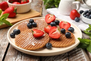 Tasty Dutch waffles (stroopwafels), mint and berries on wooden table, closeup