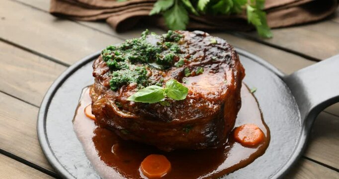 Woman adding pesto sauce to traditional ossobuco dish at wooden table, closeup. Camera moving in