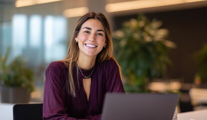 Smiling woman with a laptop in an office setting wearing a purple blouse