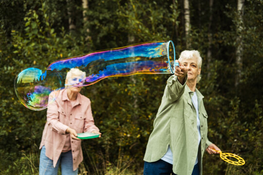 Fun in old age. Two old sisters blow soap bubbles in the park.