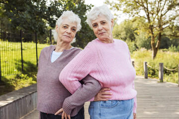 Two elderly twins hugging on a summer day in the park.
