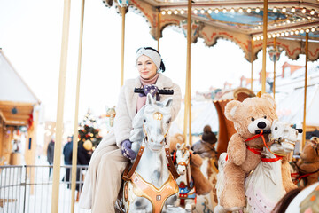 Beautiful brunette woman on a carousel. The model is saddled on a horse and having fun during the...