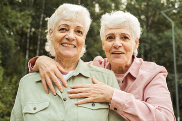 Two elderly sisters happily hugging and laughing on a summer day in the park.