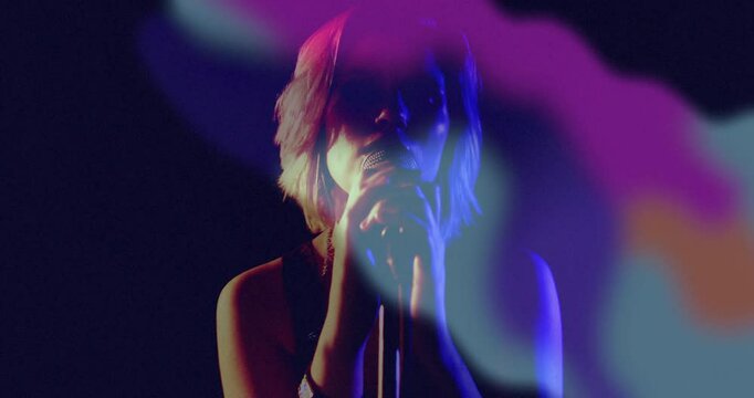 Swirling neon light projections revealing female singer holding mic and singing on music stage