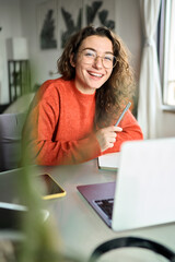 Vertical portrait of happy young woman student laughing using laptop sitting at desk studying...