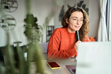 Fototapeta na wymiar Online learning concept. Young smiling pretty woman student using laptop elearning or remote working at home office using laptop computer watching webinar web course, studying online sitting at table.