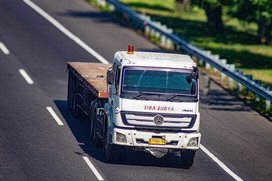 A white Mercedes Benz Axor truck from PT Siba Surya with a flatbed trailer travels on a sunny highway, symbolizing heavy cargo logistics and modern transportation, Indonesia, 17 June 2025
