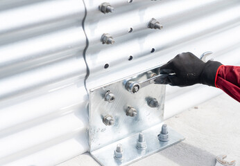 Use a wrench to tighten the bolts fixing the plate to the metal sheet wall.
