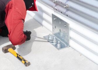 The worker is tightening the bolts on the plate to the concrete floor. A hammer is placed nearby.