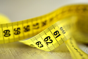 Close-up of a yellow measuring tape  on a white background, with reflection under. Unrealistic waist size ,symbolising fitness, model requirement, body idol , sewing, diet, health, body conscious.