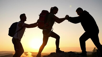 Silhouette of hikers assisting each other against a sunset backdrop.