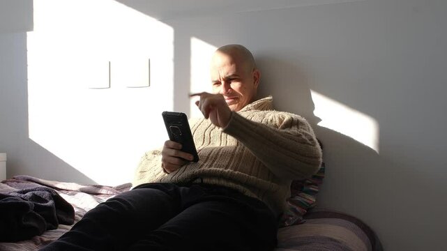 49 year old Brazilian man sitting on the bed celebrating news he just saw on his smartphone.