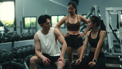 Female fitness trainers coaching male client, discussing workout strategy near exercise equipment in contemporary fitness center