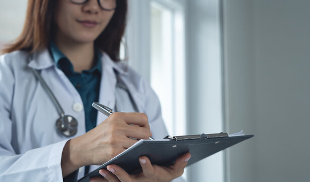 Doctor writing note or prescription on clipboard medical chart or patient history record healthcare checklist in hospital. Doctor filling life insurance document at medical clinic, close up.