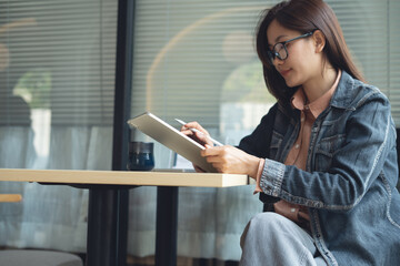 Young smart asian woman using digital tablet with laptop computer on table at coffee shop. Casual...