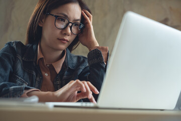 Thoughtful asian business woman thinking solving problem, searching the ideas on laptop at work,...