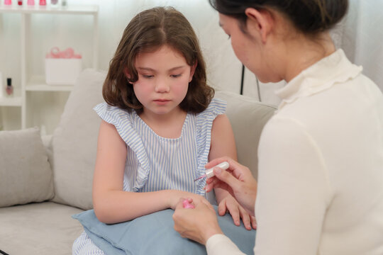 Asian single mother painting young daughter's nails during beauty session at home, nurturing bonding, trust and love shown warmly, joyful family moment, positive parenting strengthening connection