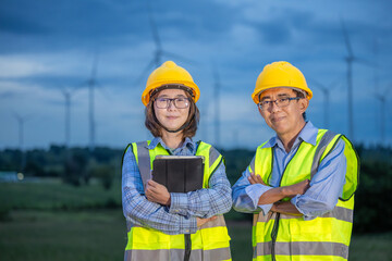 Two workers in safety vests stand in front of a wind farm
