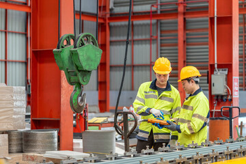 Construction site workers wea safety gear discussing plans and managing heavy industrial equipment inside a large warehouse with red steel structures