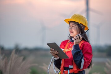 Woman engineer wearing a yellow hard hat and a red jacket is holding a tablet
