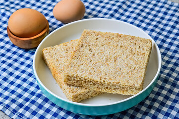Close up view of whole wheat sliced bread on plate with two chicken eggs isolated on napkin background. blue, white. 