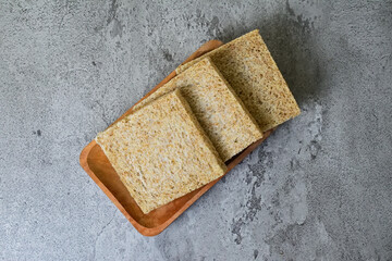 Top view of whole wheat sliced bread on long wooden plate. grey or gray cement as background. High angle, above, close up.