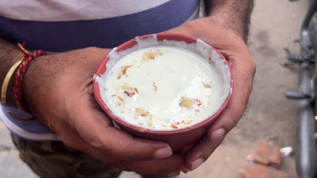 A man holding a glass of Delhi styled Lassi with dry fruits