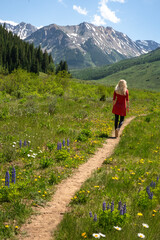 Blonde Woman Hiking in Red Dress Through Scenic Mountain Meadow