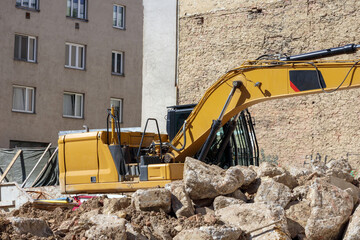 
a large, yellow excavator located on a construction site among rubble and two buildings – one...