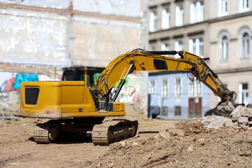 
A large, yellow excavator is located on a construction site with piles of sand and rubble, with...