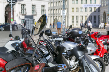 
A row of various motorcycles and scooters parked on a paved square in an urban setting with...