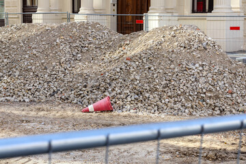 
A scene of a construction site with two large piles of gravel or rubble, a red cone lying in the...