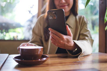 Closeup image of a woman holding and using mobile phone while drinking coffee in cafe