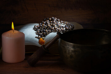 Tibetan singing bowl, rosary beads, and a lit candle create a peaceful atmosphere on a wooden surface