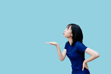 Young Asian woman playfully blowing a kiss against a solid blue background during a bright and...