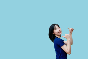 Cheerful young Asian woman signals with thumbs up against a solid blue background in a bright and...