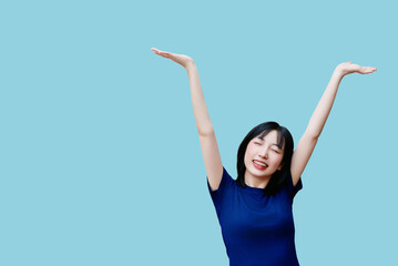 Smiling Asian woman celebrating joyfully with arms raised in a cheerful pose against a light blue...
