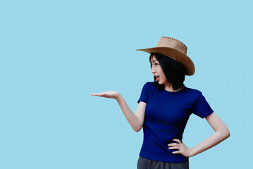 Woman wearing a straw hat poses against a light blue background showcasing enthusiasm and style in a casual outfit