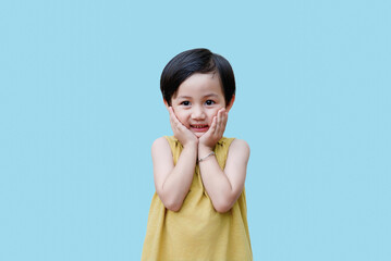 Young Asian child expresses joy with hands on cheeks against a bright blue background, showcasing a...