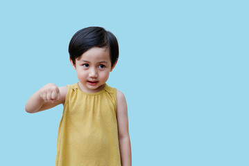 Young child with short black hair making a fist and smiling against a light blue background,...