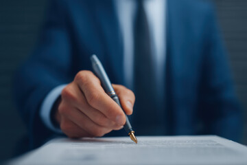 Businessman hand holding pen signing contract document, formal agreement, professional setting, focus on signature process