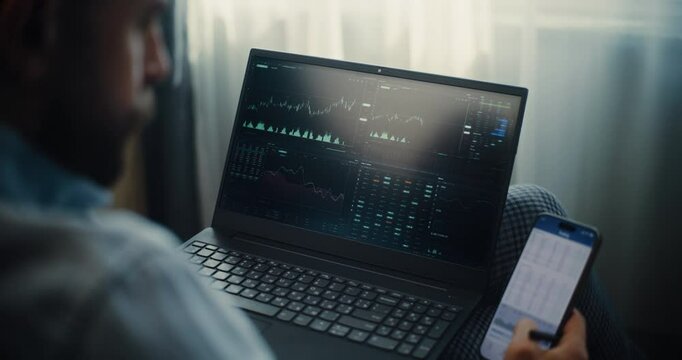 Close Up of Stock Exchange Trader Monitoring Real-Time Stocks and Exchange Market Charts in Online Trading App Using Smartphone and Laptop. Investment Agent Working in Office of Financial Agency.