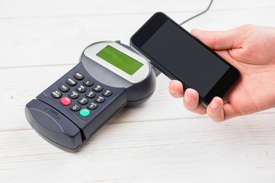 Hand holding mobile phone with credit card reader on table