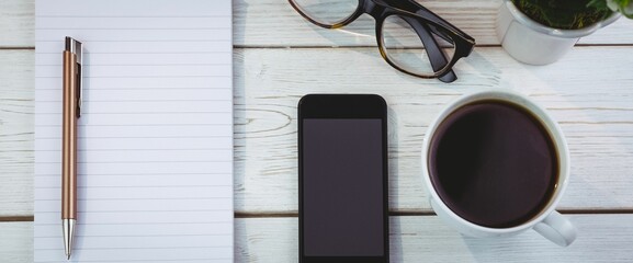 Pen on book with smartphone and coffee cup by eyeglasses at desk