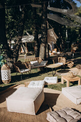 Outdoor boho-style lounge area with soft floor cushions, low tables, and rattan chairs under trees, perfect for laid-back weddings, events, or gatherings in nature.