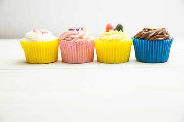 Cupcakes are being shown in flat design on white wooden tabletop with colorful liners and frosting