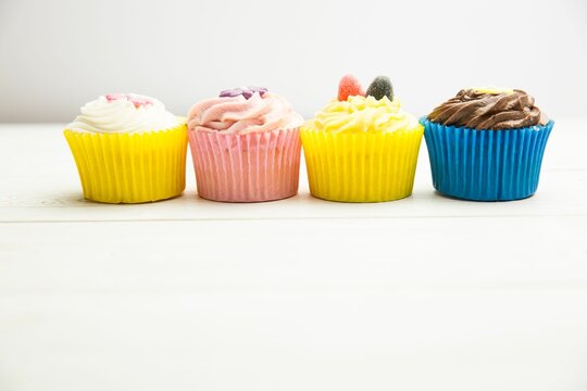 Naklejki Cupcakes are being shown in flat design on white wooden tabletop with colorful liners and frosting