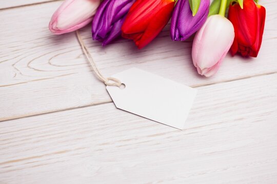 Fototapeta Flat design is showing tulip blossoms resting on pale wooden tabletop with blank white gift tag