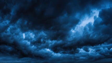Obraz premium Dramatic sky filled with dense dark blue-black clouds, moody atmosphere, impending storm, patches of lighter blue, intense weather event, powerful cloud cover.