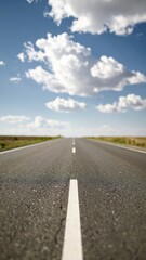 Obraz premium A straight, empty road stretches into the horizon beneath a bright blue sky dotted with white clouds.